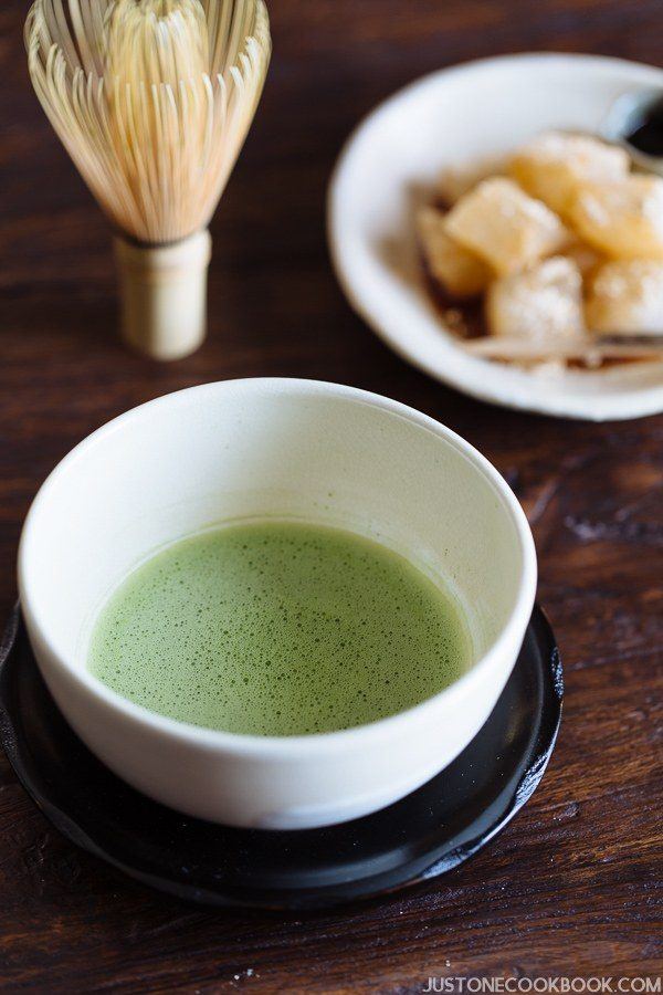 Matcha, Japanese green tea in a white tea bowl and a small plate of mochi on the wooden table.